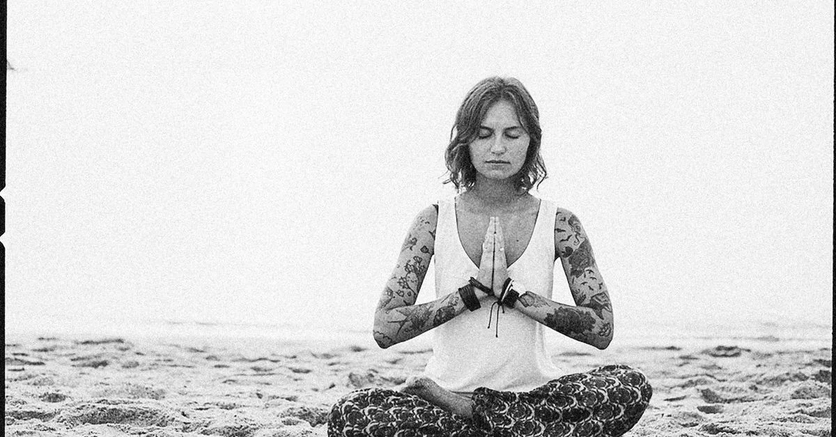 Une femme en position de méditation sur la plage, illustrant la pleine conscience et la paix.